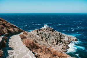 White and blue Church perched on a rock next to the ocean in Sifnos, Greece